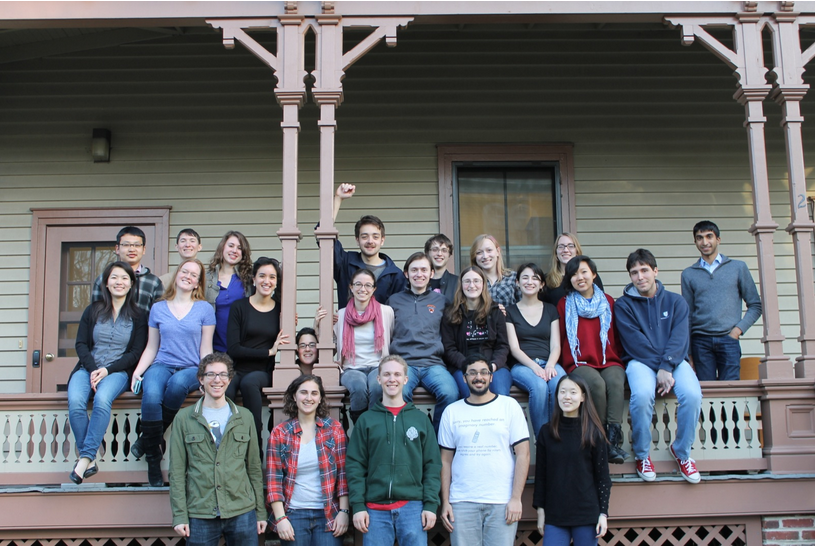 Many students in front of a wooden house