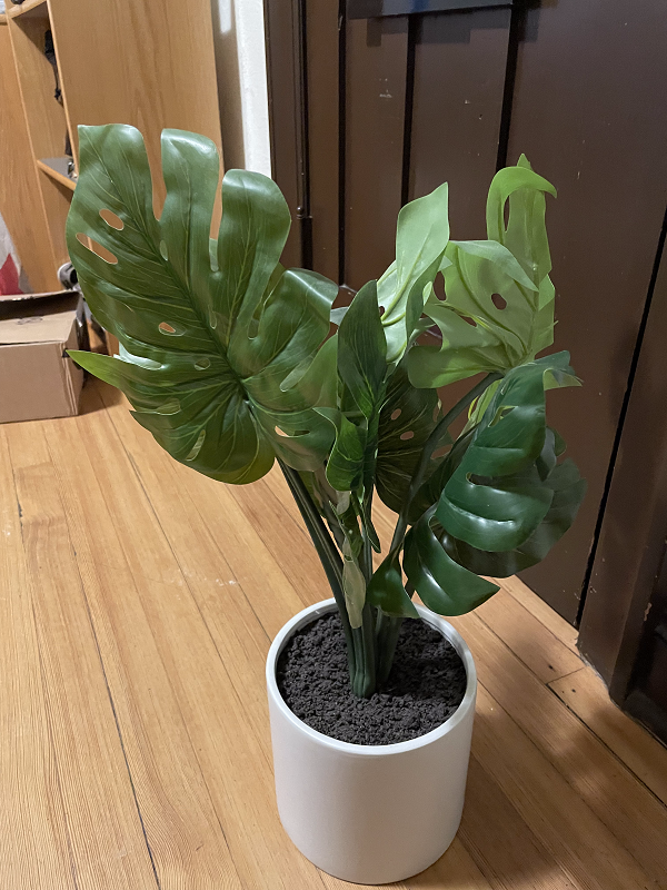 A fake plant that has large, green leaves and is in a white pot.