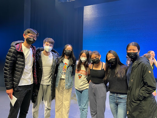 Seven people stand on a stage, in front of blue lit backdrop