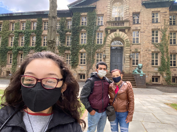 A family of three poses in front of Nassau Hall wearing face masks.
