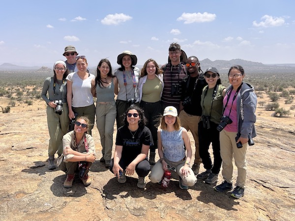 group photo of 13 smiling people in a savannah landscape