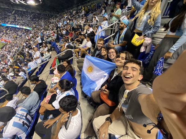 5 people smiling to a selfie in a stadium