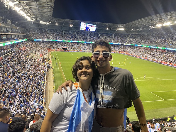 A girl and a boy smiling in front of a soccer field