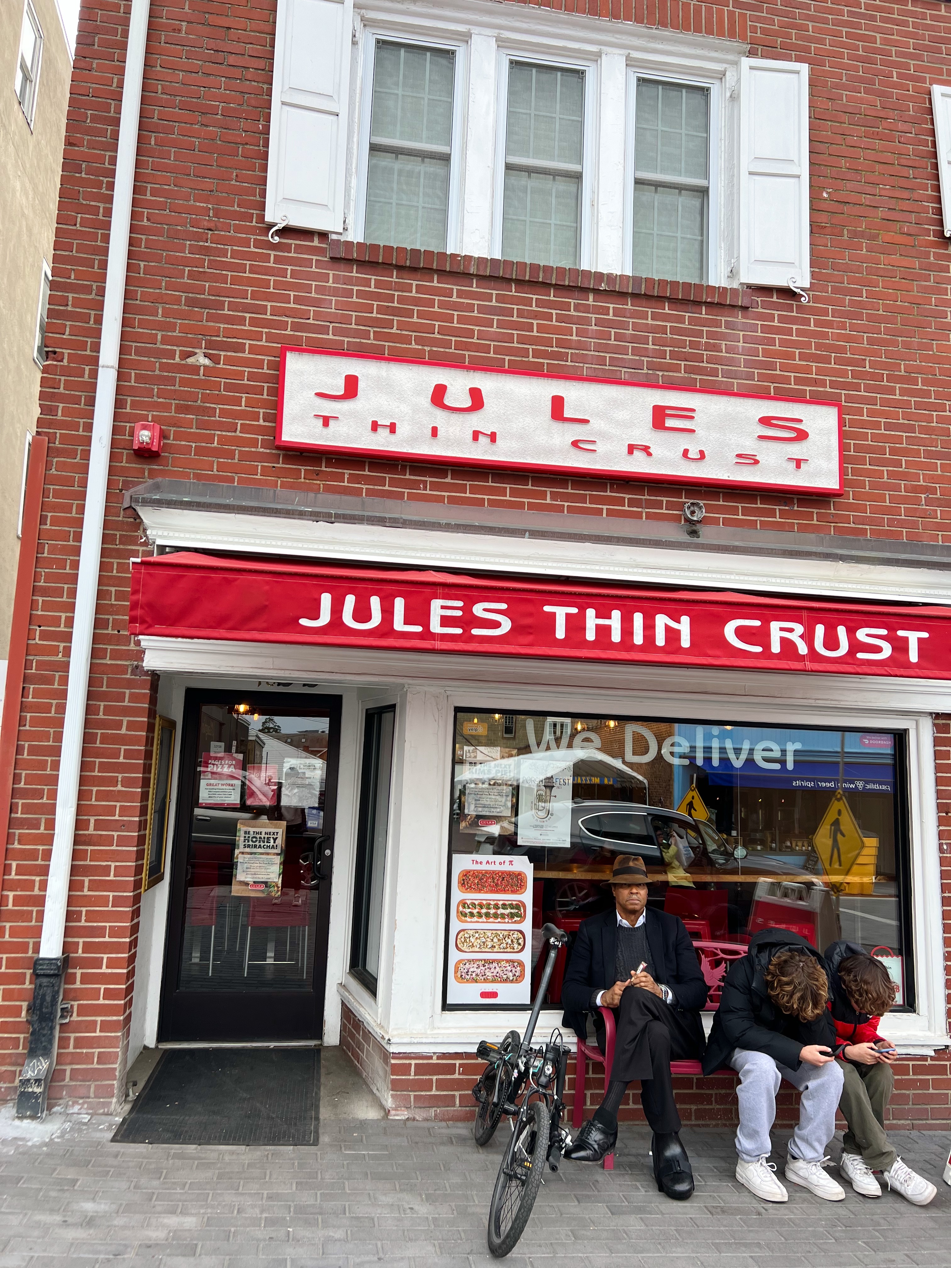Exterior of Jules Thin Crust, red brick building with white shutters and trim, a Jules Thin Crust sign and red awning