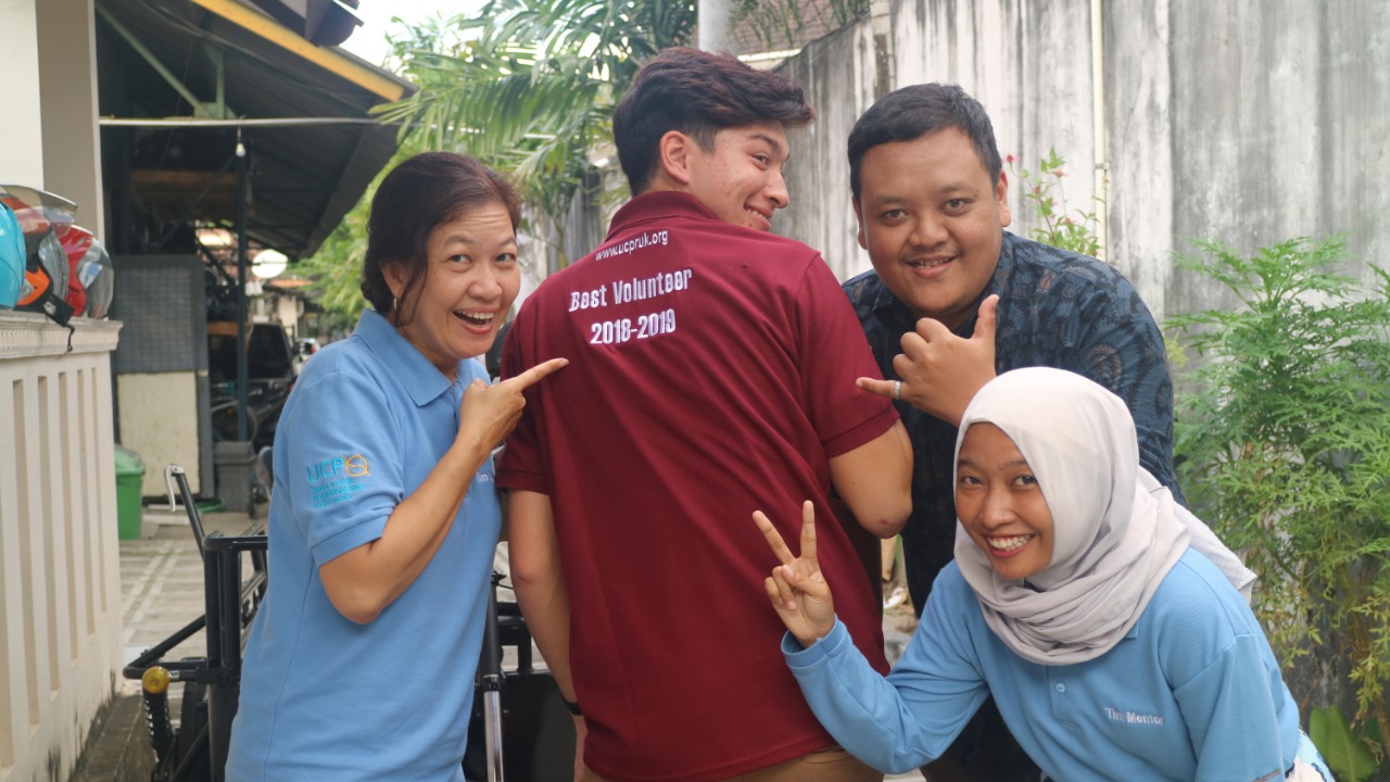 Oscar turns to lookback at the camera, posed with three coworkers, his shirt reads "best volunteer 2018-2019" 
