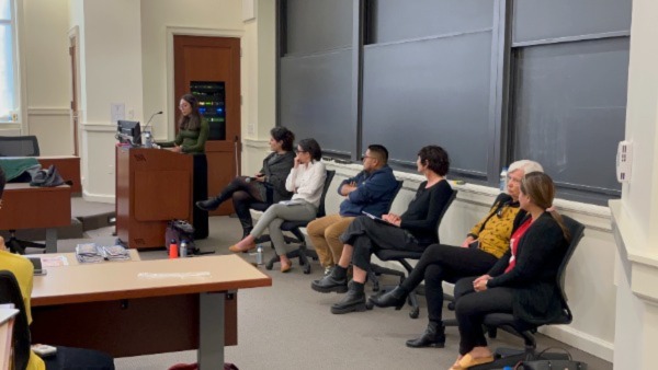 Princeton student speaks at podium next to six seated panelists at the front of a classroom.