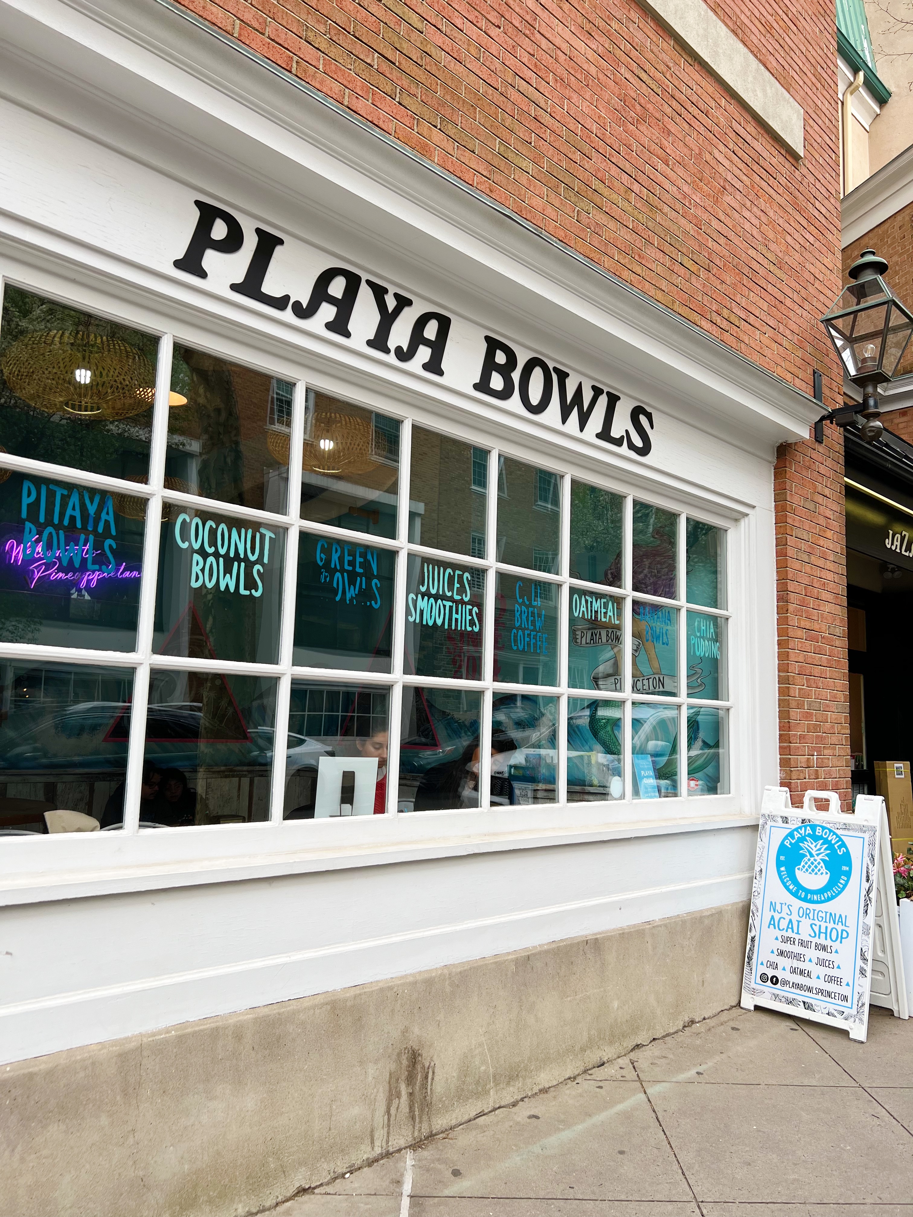 Exterior of Playa Bowl, red brick building with white window trim and black letters reading "Play Bowls"