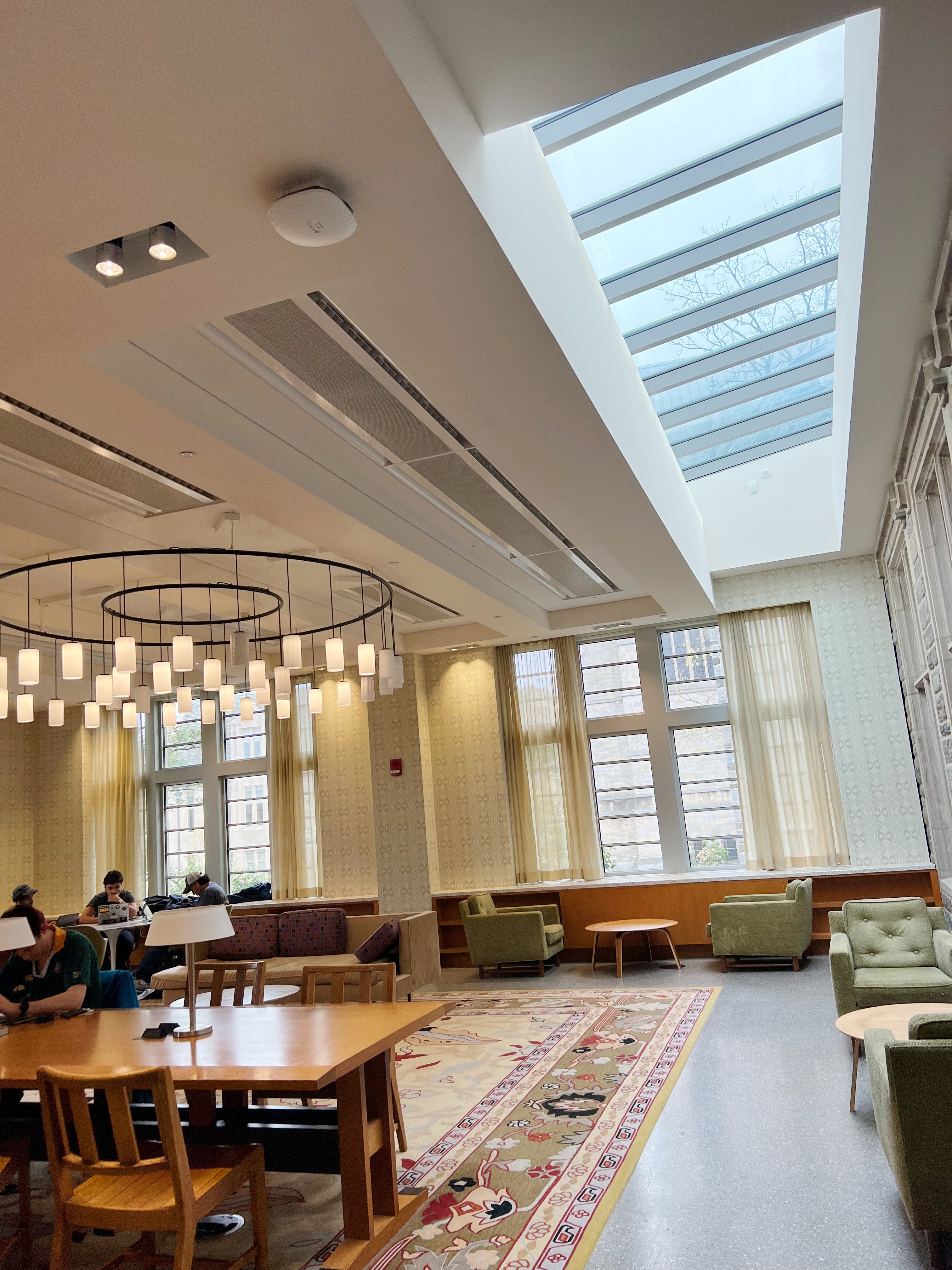 room with reading tables, arm chairs, large windows and sky lights and chandelier