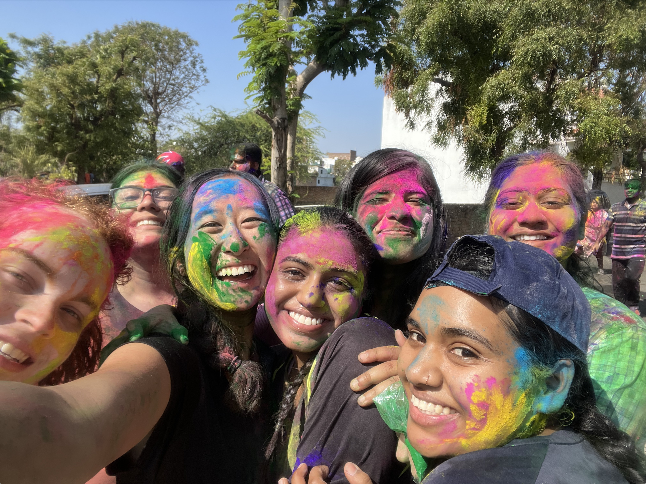 Group of young women pose for a selfie with colorful powder on them from Holi celebrations