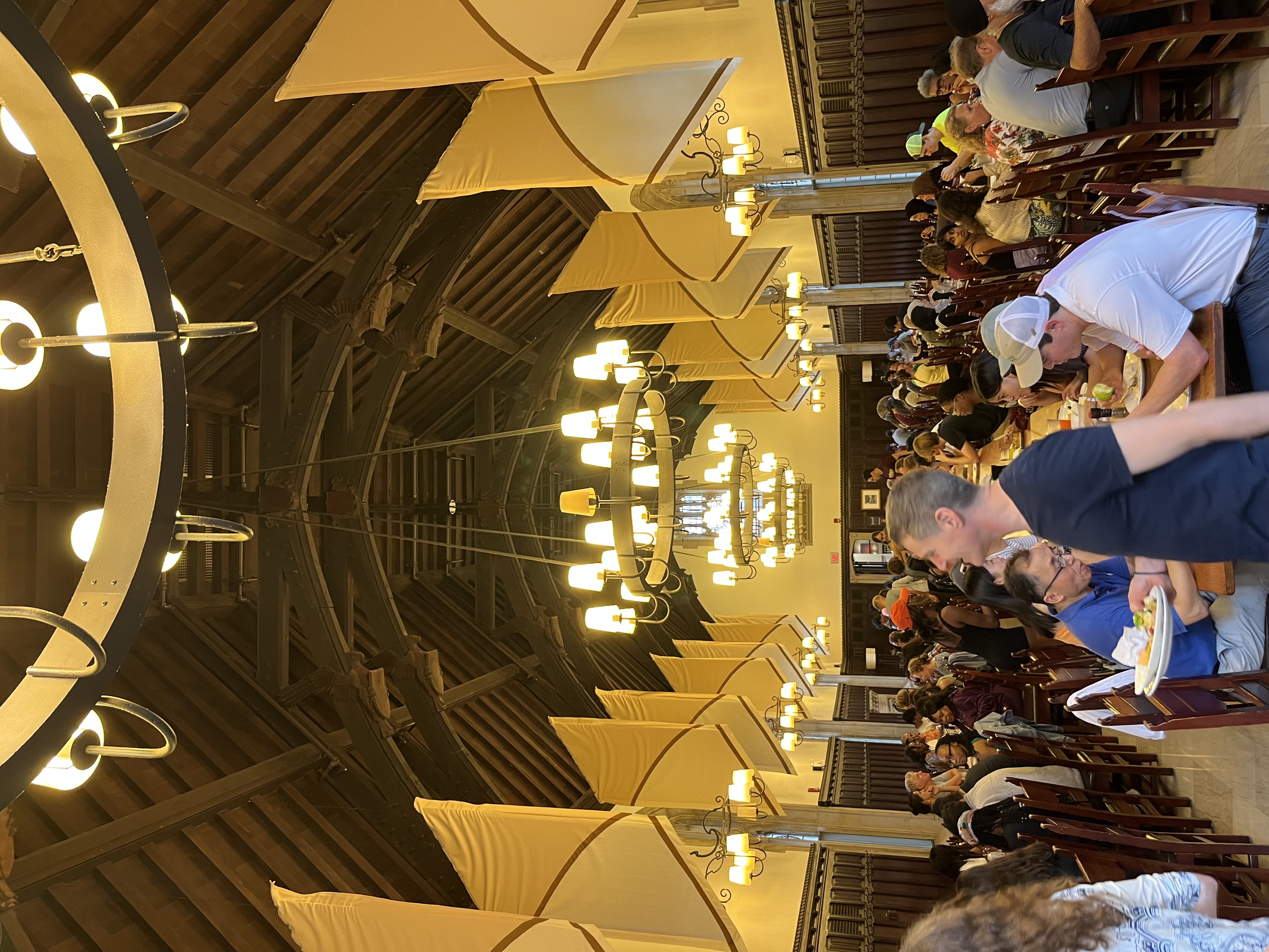 a picture of a dining hall with chandeliers and wooden benches. 