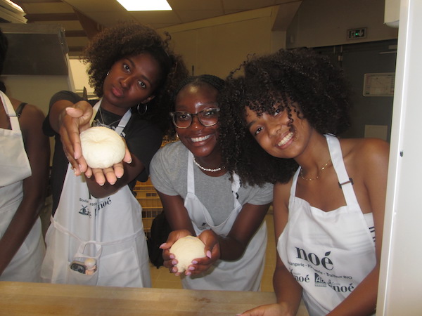 Three students holding bread dough in a boulangerie.