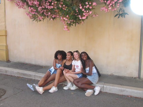 Four girls sitting on a sidewalk, underneath a flower tree.