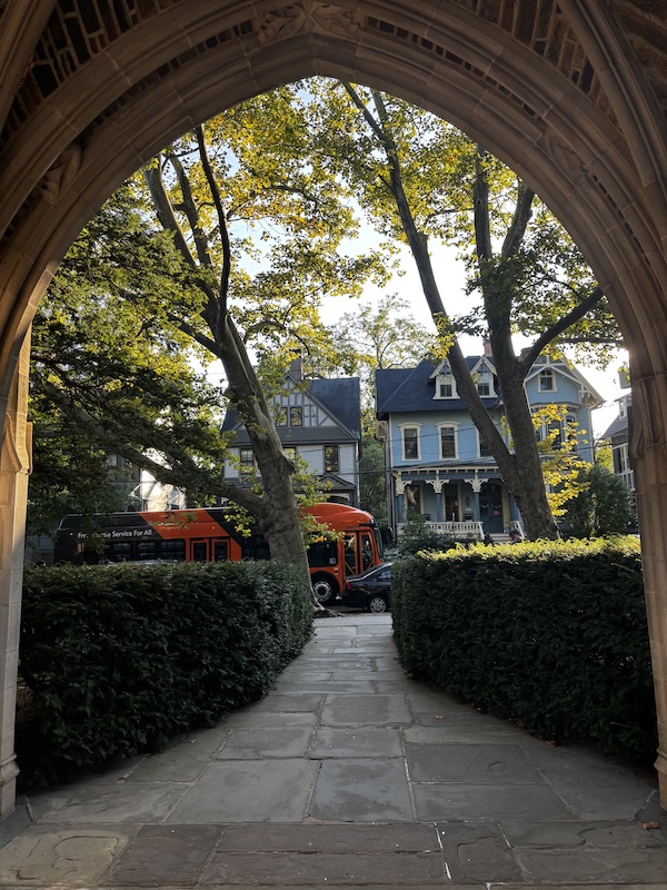 An archway in late-afternoon, through it one can see houses, cars, and trees