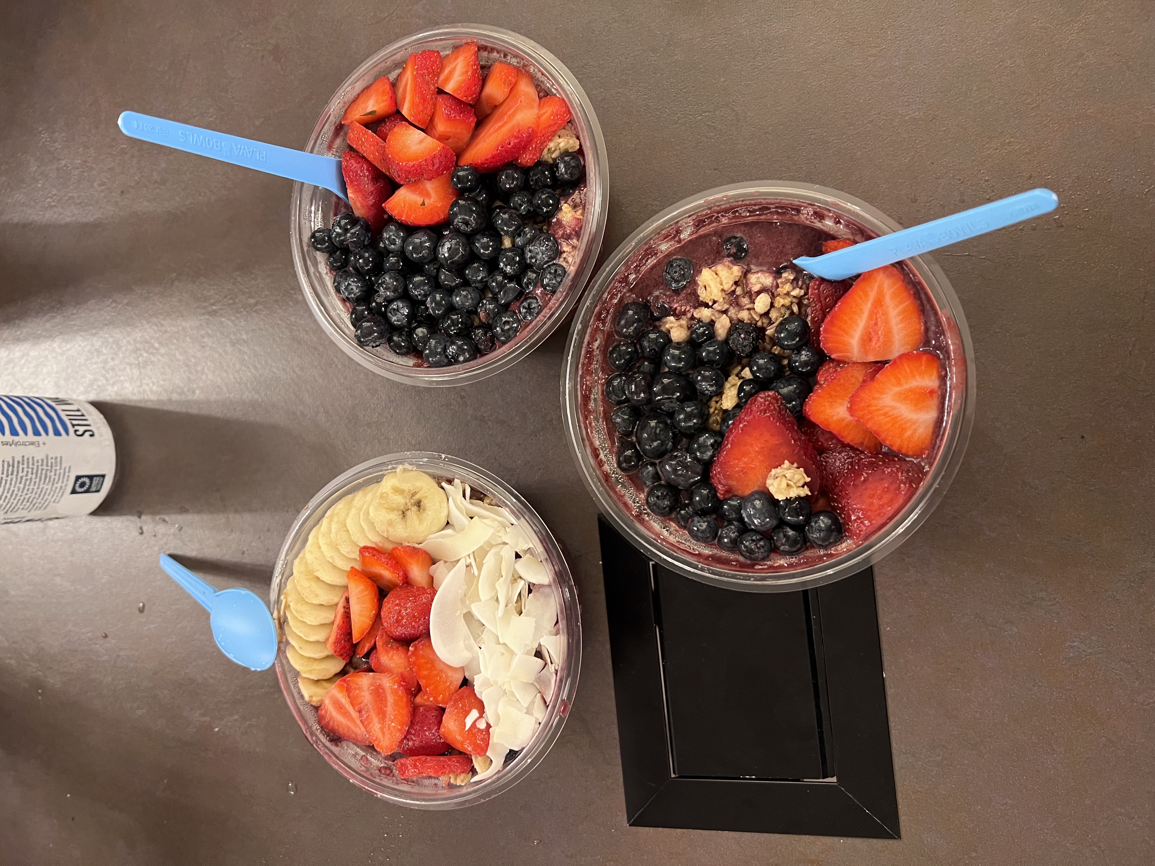 three bowls of acai bowls with strawberry, blueberries, banana slices, and coconut flakes