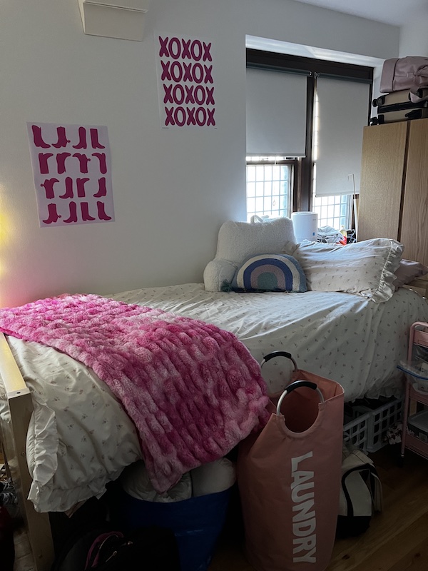 A bed in a dorm room --- a pink blanket and colorful pillows sit on top