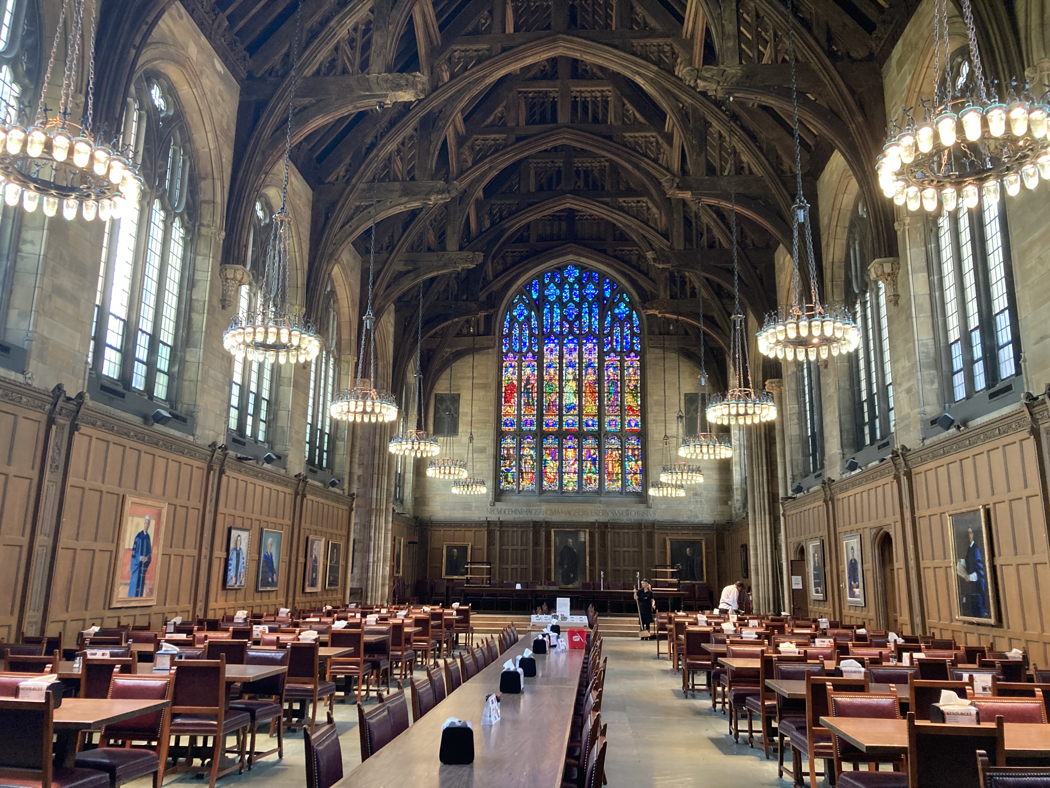 With a stained glass window in the middle, there are floating chandeliers and long wooden tables on each side. 