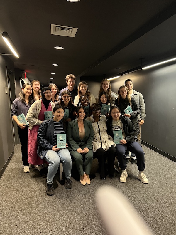 A group of people posing for a photo and holding up turquoise books