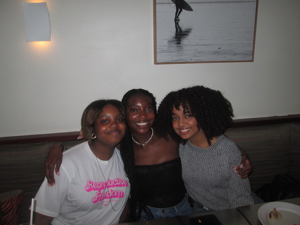 Three girls sit in a restaurant booth, smiling