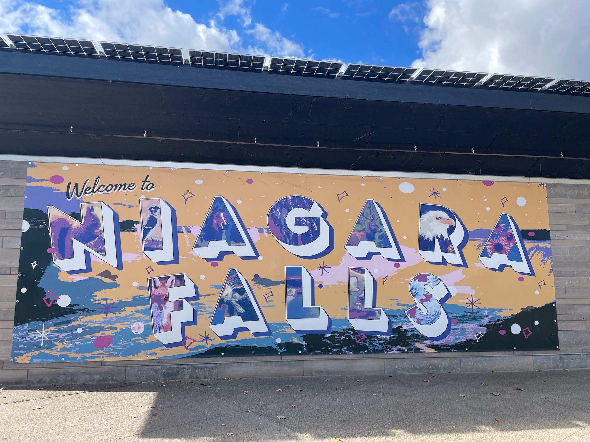 a wall painted with a yellow background and blue/black text reads "Welcome to Niagara Falls"