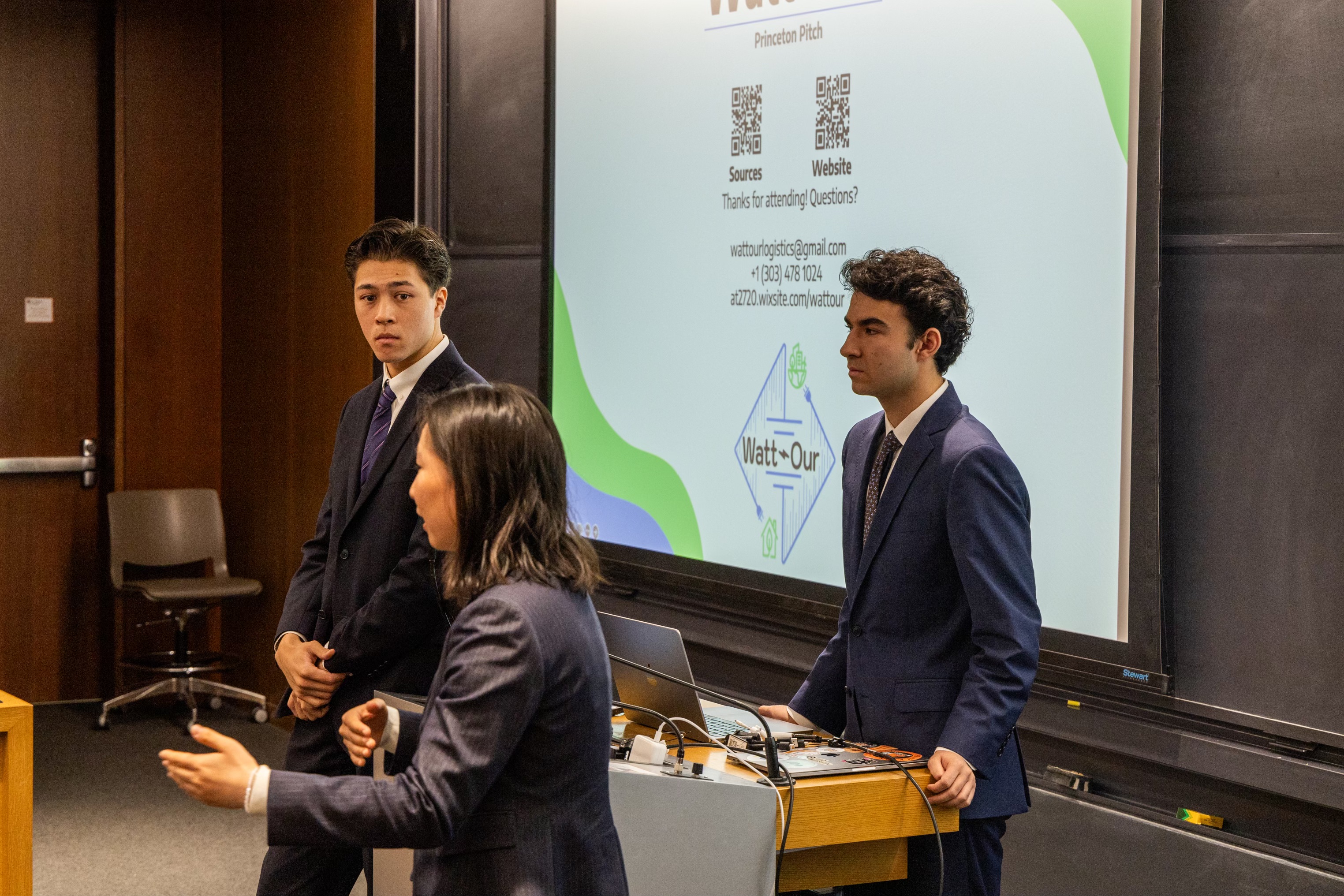 Three students dressed in suits presenting a powerpoint.