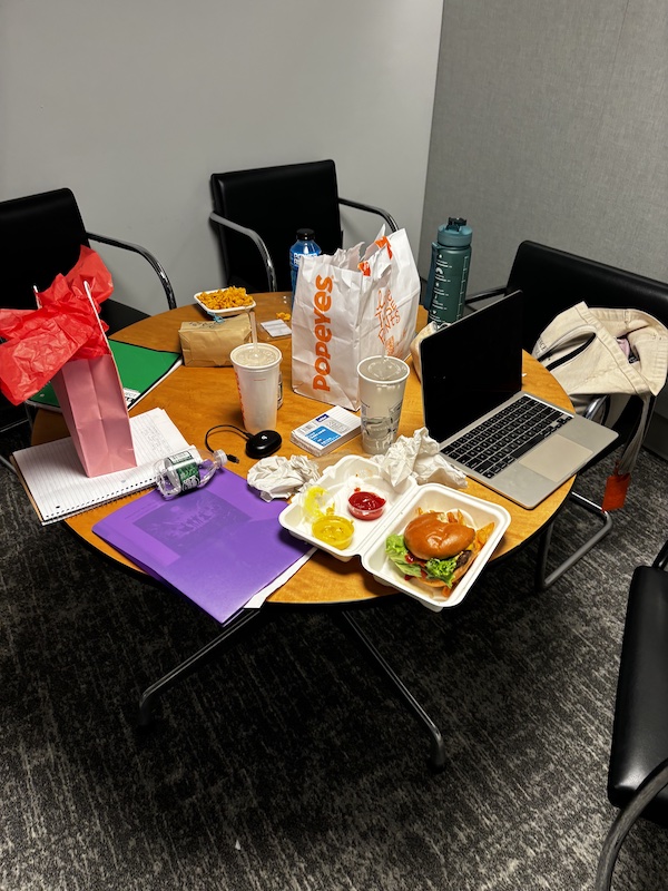 A cluttered table, full of food and study materials