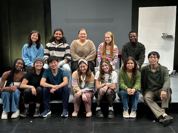 A group of students sit, smiling, on a stage