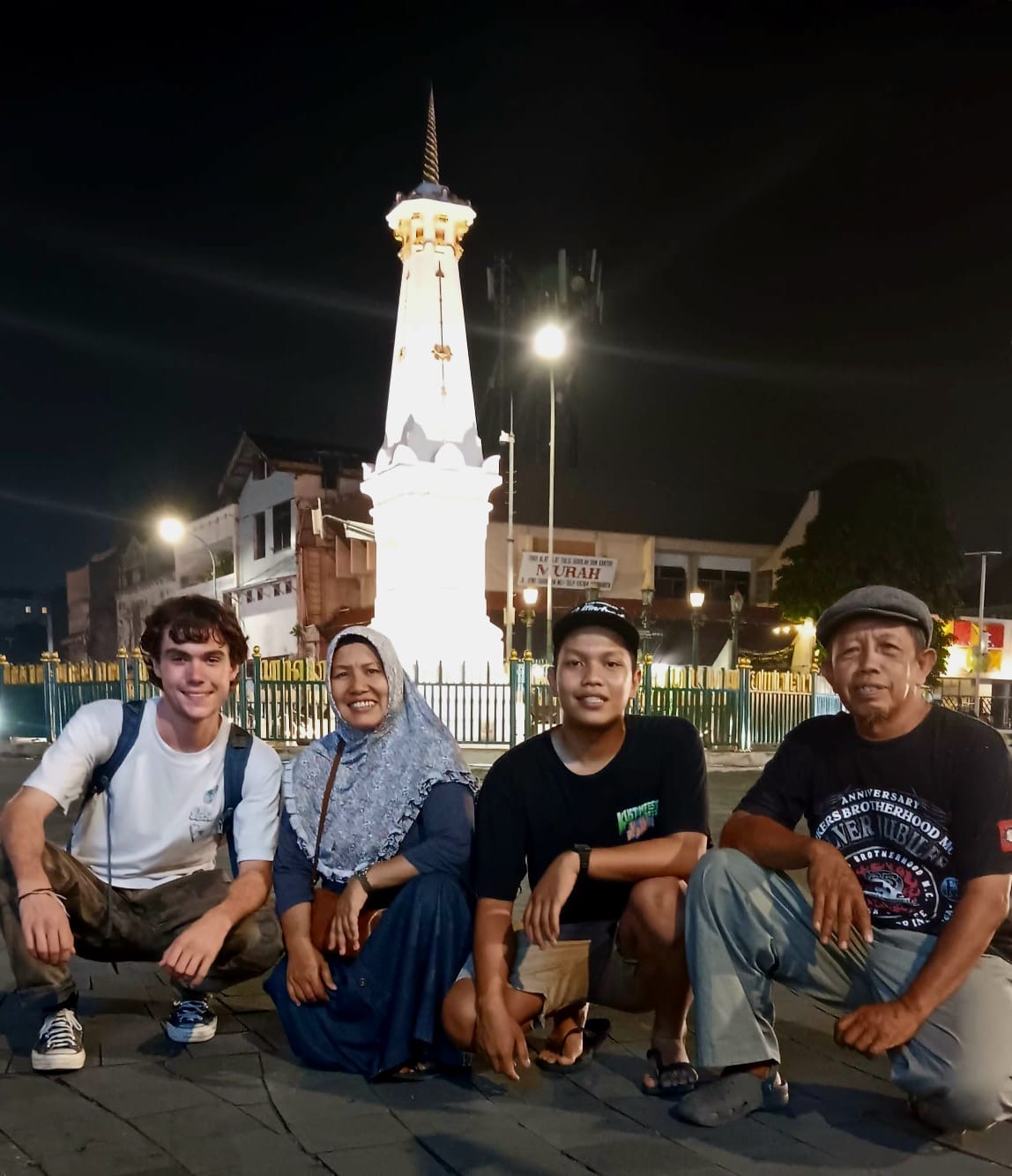 Four people crouch in front of the Tugu (Monument) Yogyakarta