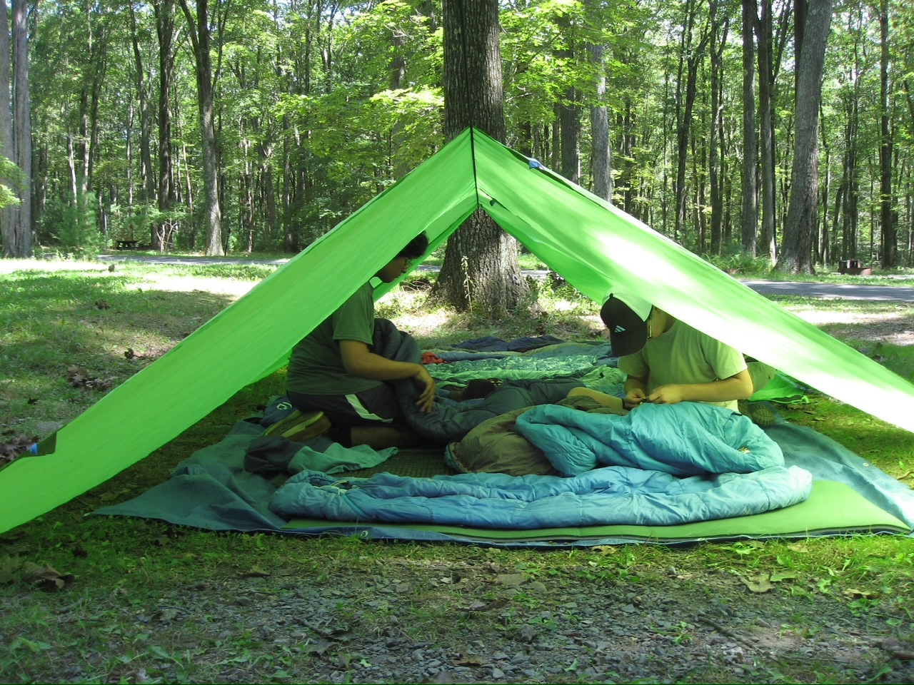 Two students sit under a tarp tent with open sides