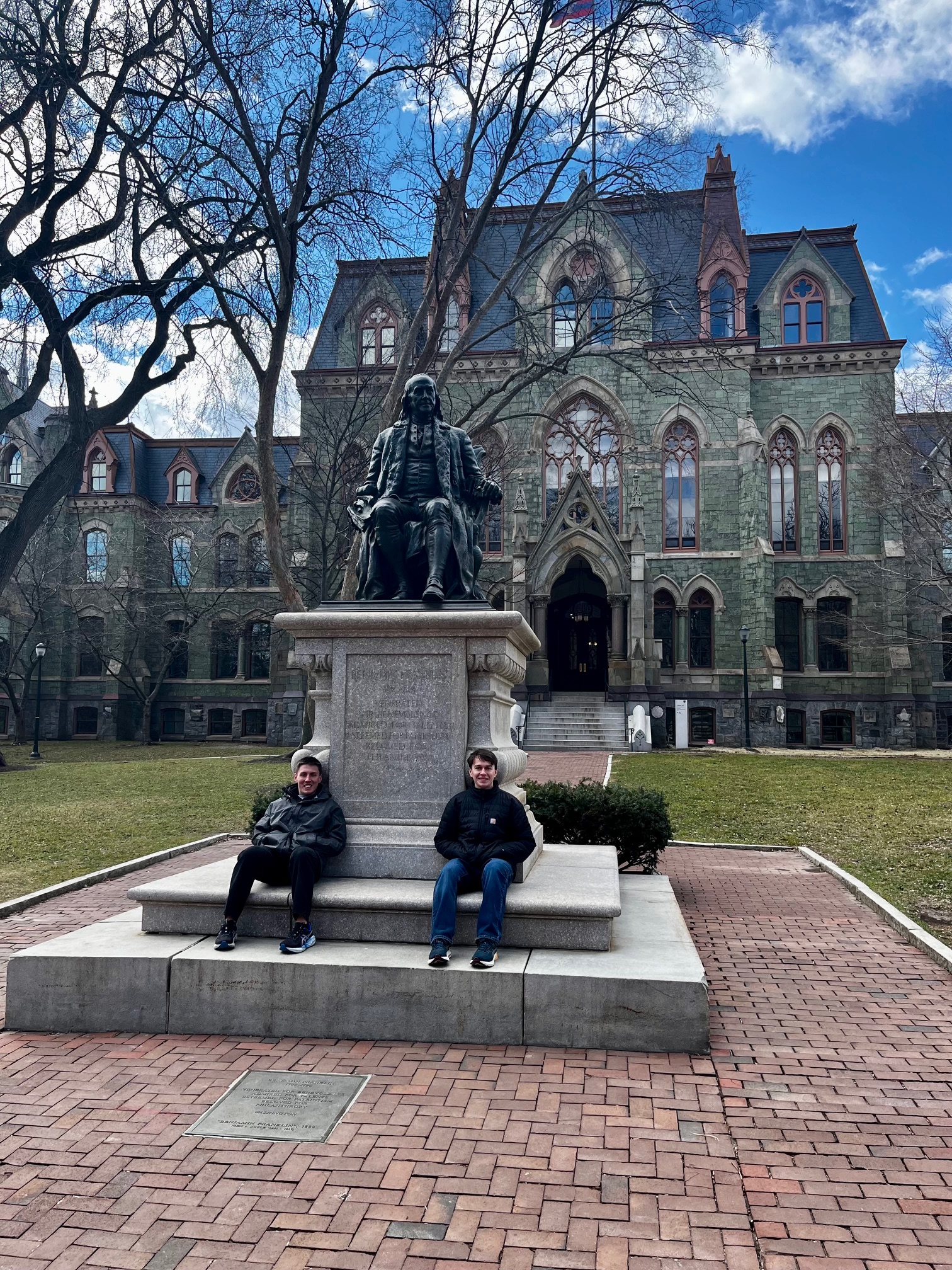 Drew Sloan and his brother sit in front of Benjamin Franklin statue at the University of Pennsylvania