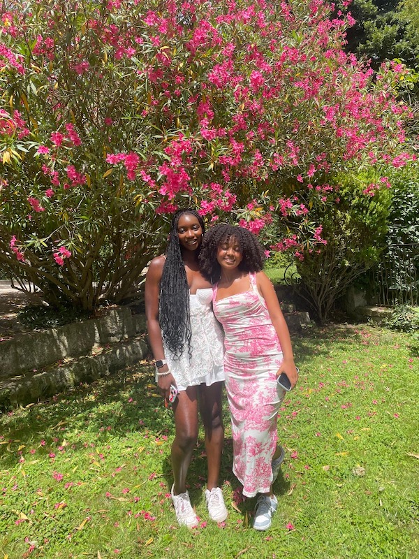 Two girls smile, in front of a blossom tree