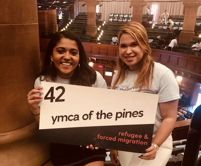 Daniela with a friend holding a sign that reads "42 YMCA of the pines, refugee & forced migration"