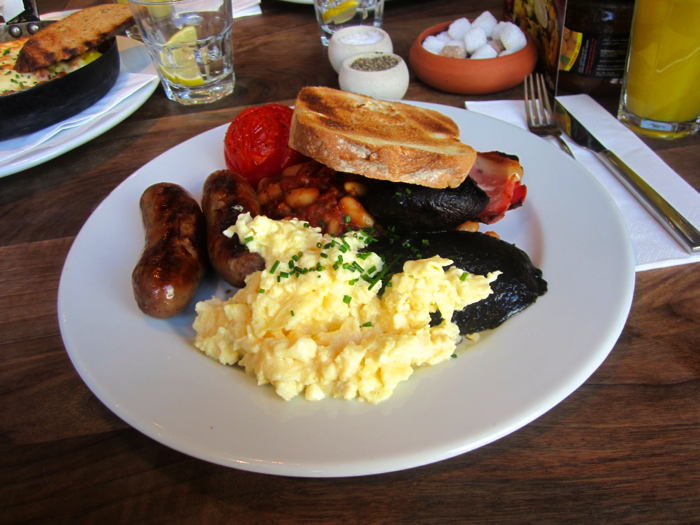 A picture of a typical English Breakfast: eggs, bacon, beans, mushrooms, tomatoes, sausages, and toast.