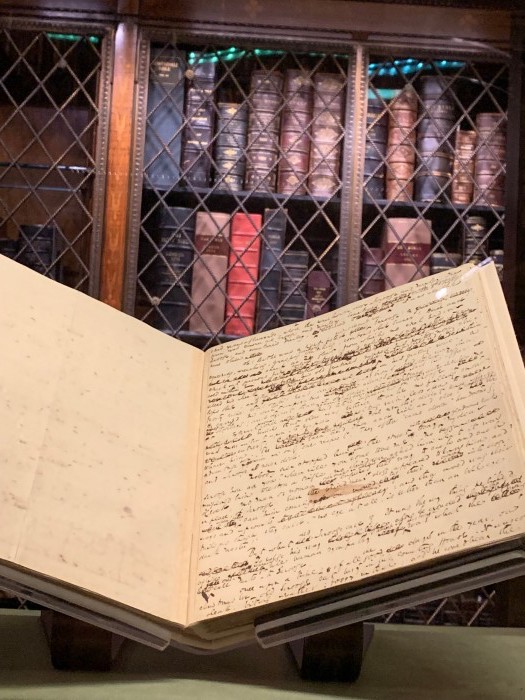 Open manuscript in Morgan Library with shelves of books in the background