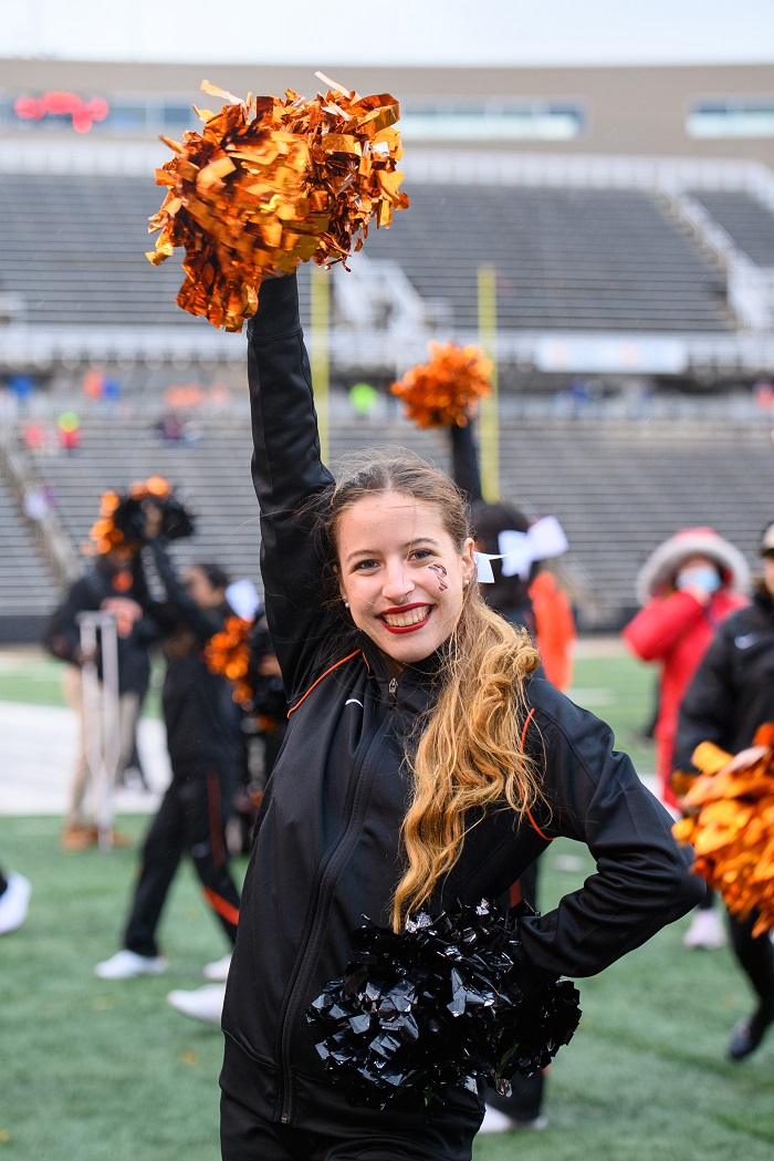 Mia in her cheer uniform with orange and black pom-poms