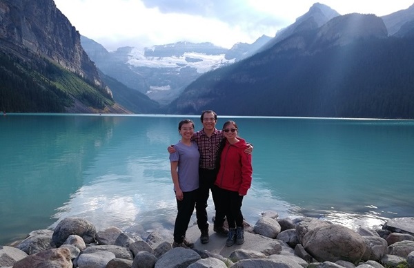 Myself, my dad and my sister standing on rocks at the edge of a lake with snowy mountains in the background