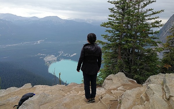 Me, a girl wearing a black sweater and black pants, standing on a mountain looking out at a lake and mountain range