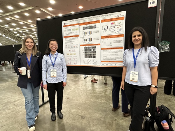 Three people standing in front of a black bulletin board with a research poster attached