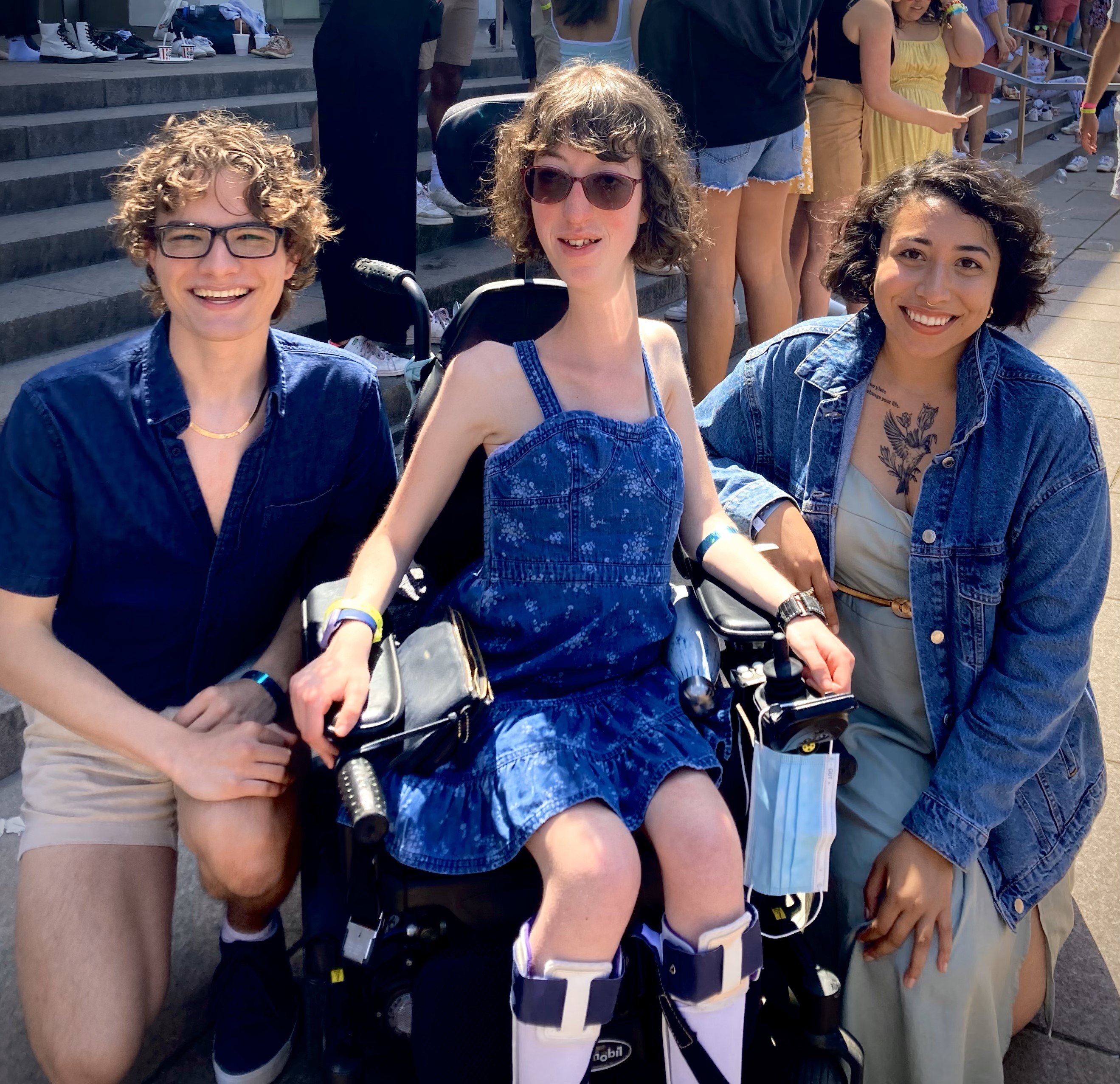 Harper (left) with two other fellows; Harper and one other fellow are squatting on a paved patio, the middle fellow is using a wheelchair