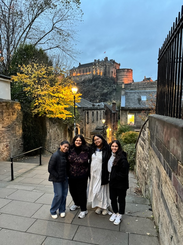 Four women standing at the top of a set of stairs, in front of a castle.