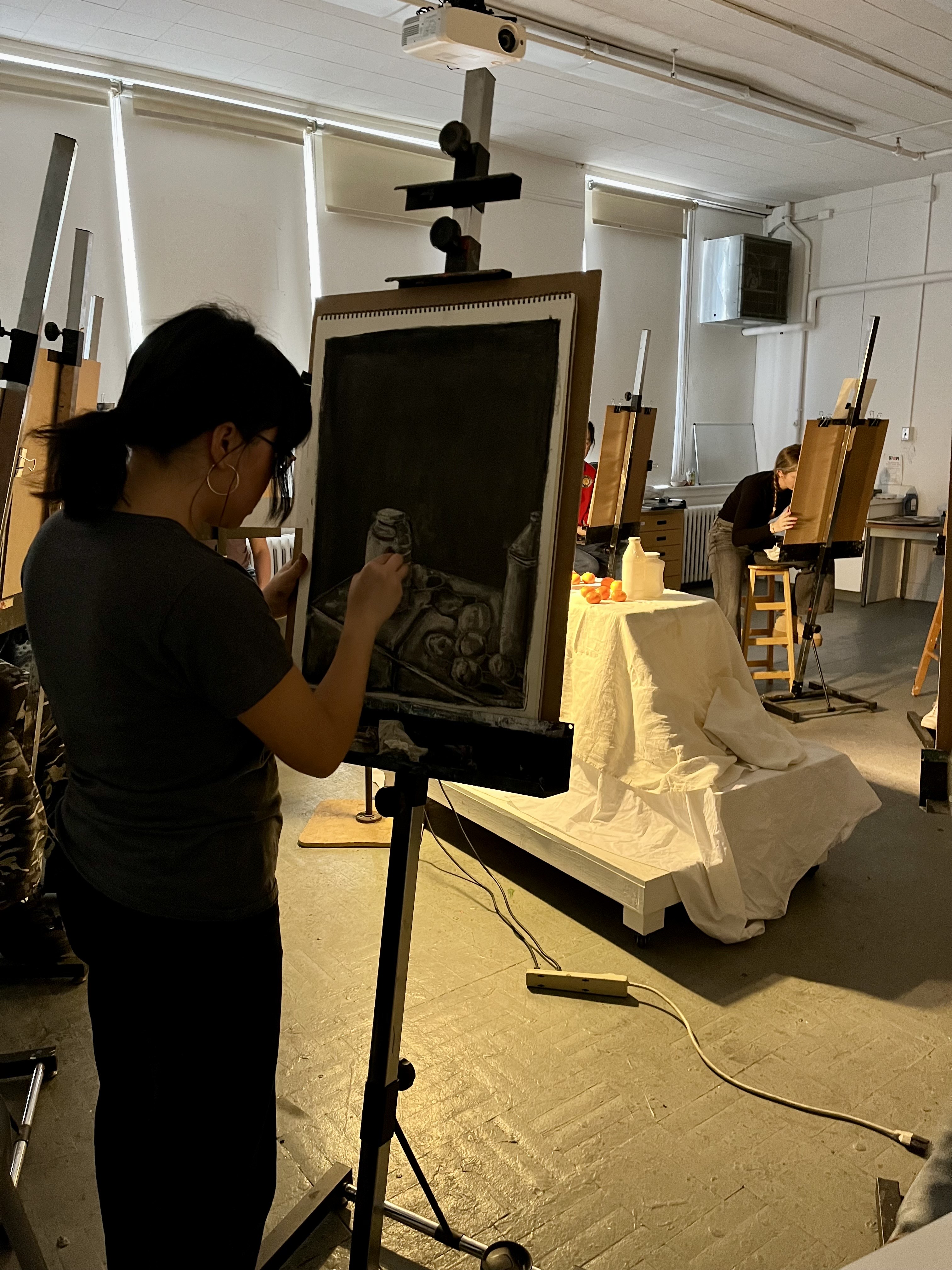 Student stands drawing at an easel 