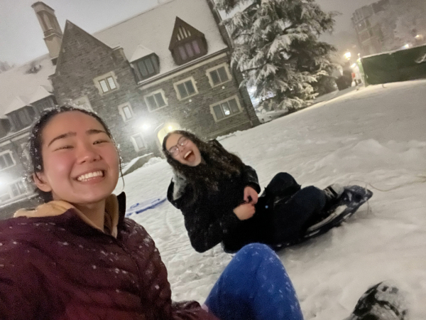 Two Princeton students smiling on sleds outside of Whitman College.