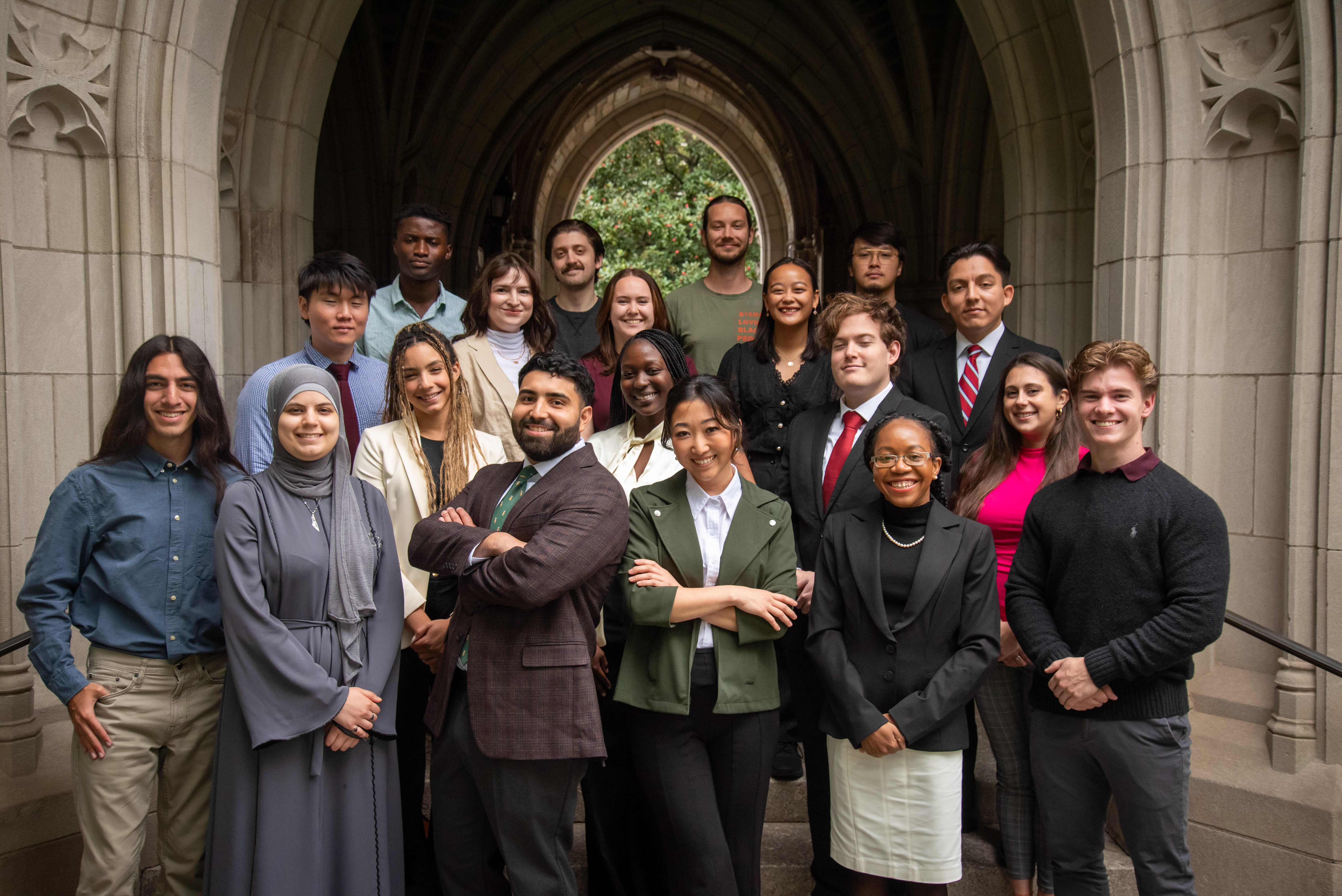 19 transfer students dressed formally pose in front of a campus gothic archway