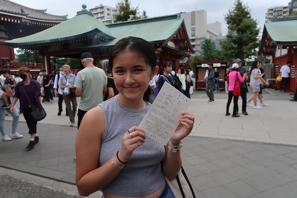 student posing with paper in front of Japanese temple