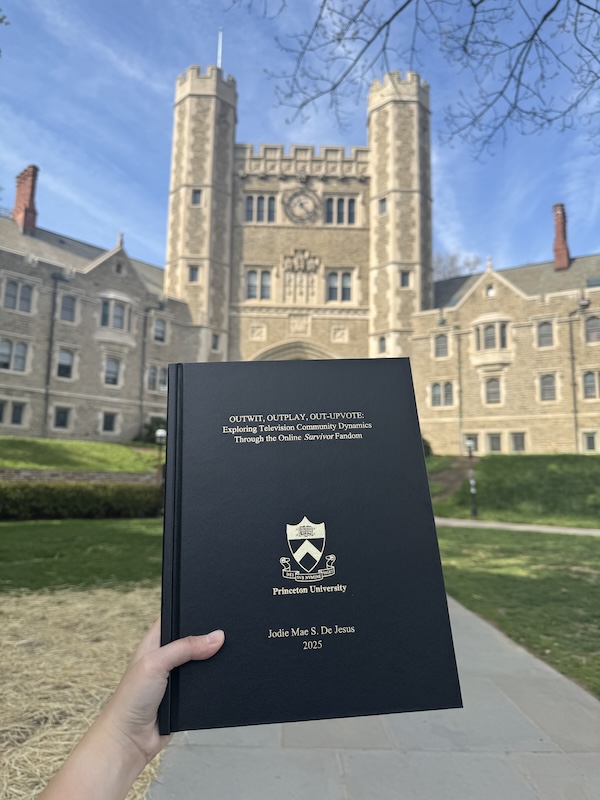 Printed senior thesis held up in front of Blair Arch