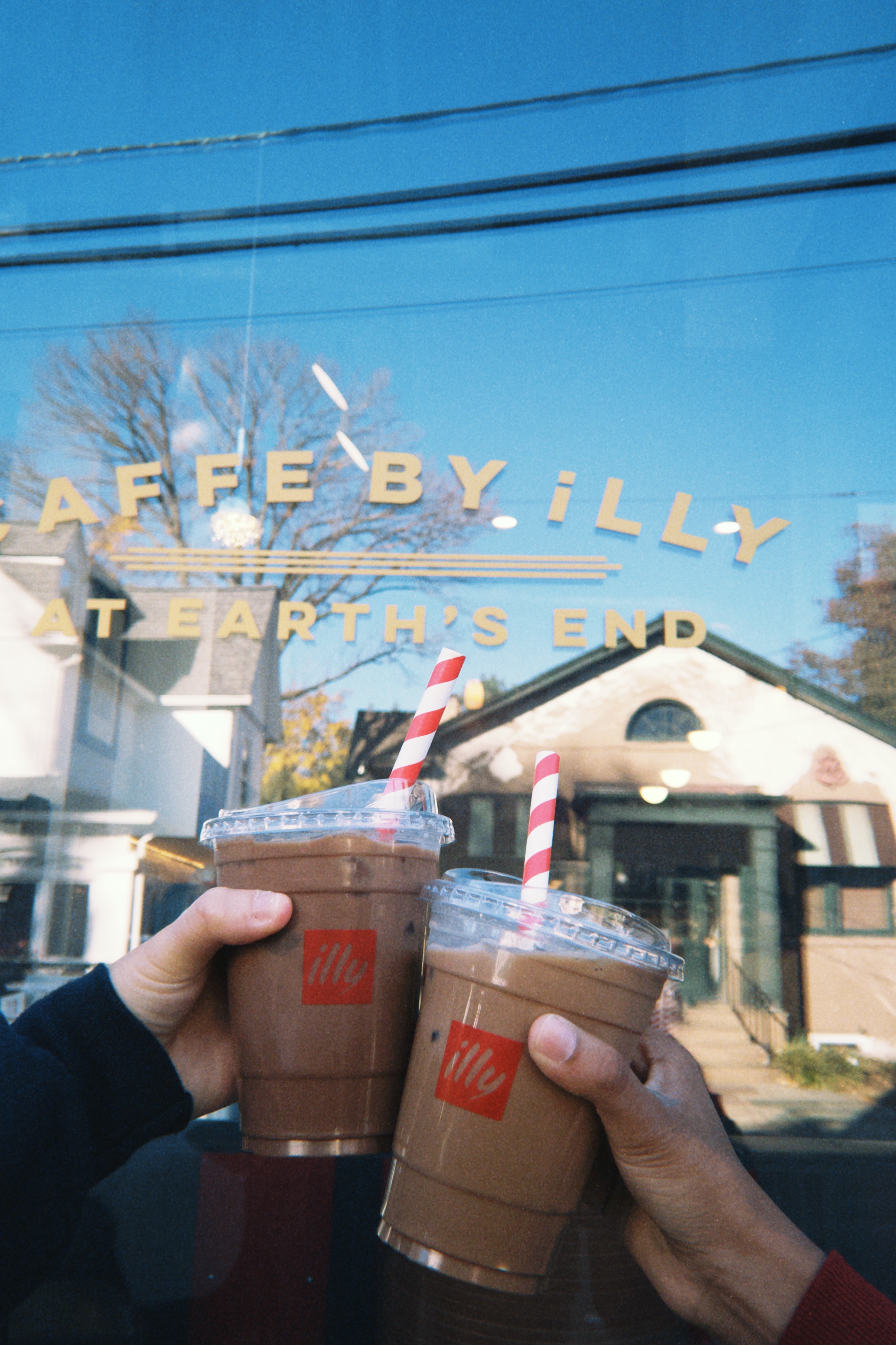 Coffees in to-go cups being cheers'd together outside a coffee shop