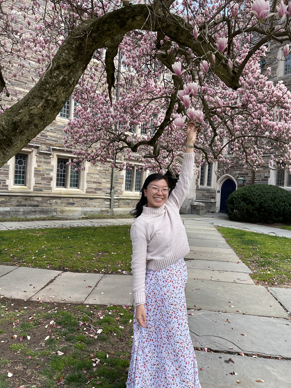 A photo of myself reaching up to touch a branch of a blooming magnolia tree
