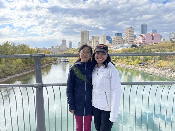 Two people standing on a bridge over a turquoise river with a city skyline in the background