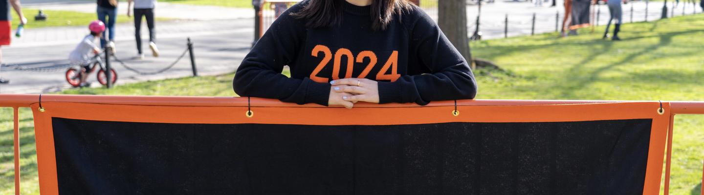 A student standing in front of a black banner with the words EAS written on it in orange. The student is smiling.
