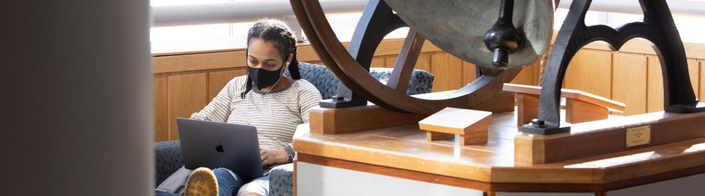 Student with a mask sitting in a chair with laptop