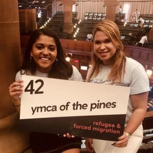 Daniela with a friend holding a sign that reads "42 YMCA of the pines, refugee & forced migration"